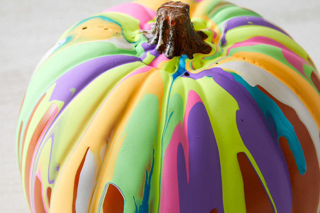 Pumpkin with multicolored paint dripped onto it.